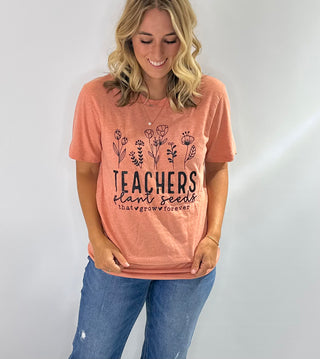 Peach graphic t-shirt with black text that reads Teachers Plan the Seeds that grow forever in bold lettering 