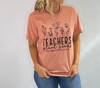 Peach graphic t-shirt with black text that reads Teachers Plan the Seeds that grow forever in bold lettering 