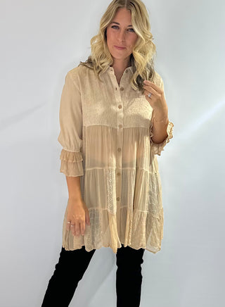 Long flowy blouse with a tiered patchwork design, translucent bodice, 3/4 ruffle sleeves, embroidered and jacquard details and a button front with collar in a soft beige. 