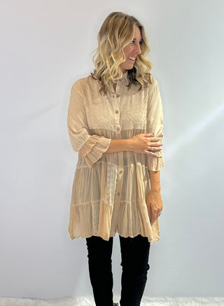 Long flowy blouse with a tiered patchwork design, translucent bodice, 3/4 ruffle sleeves, embroidered and jacquard details and a button front with collar in a soft beige. 