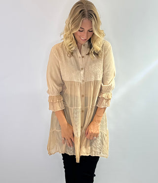 Long flowy blouse with a tiered patchwork design, translucent bodice, 3/4 ruffle sleeves, embroidered and jacquard details and a button front with collar in a soft beige. 