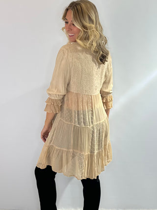 Long flowy blouse with a tiered patchwork design, translucent bodice, 3/4 ruffle sleeves, embroidered and jacquard details and a button front with collar in a soft beige. 