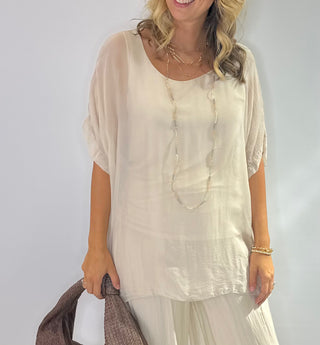 Oversized cream silk blouse with short sleeves, scoop neck, double-layer front and tie-back detail.