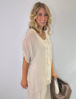 Oversized cream silk blouse with short sleeves, scoop neck, double-layer front and tie-back detail.