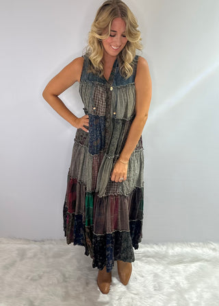 A long boho patchwork maxi duster with a hood, sleeveless design, full button front closure, drawstring ties, and tiered flowy silhouette
