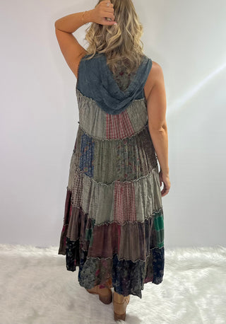 A long boho patchwork maxi duster with a hood, sleeveless design, full button front closure, drawstring ties, and tiered flowy silhouette