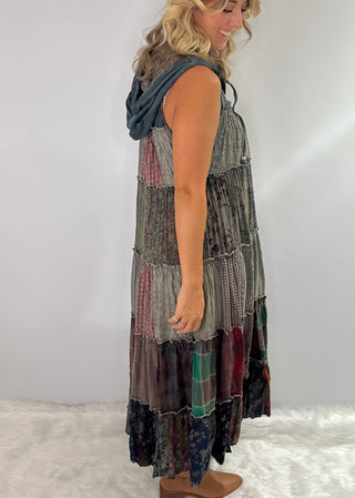 A long boho patchwork maxi duster with a hood, sleeveless design, full button front closure, drawstring ties, and tiered flowy silhouette