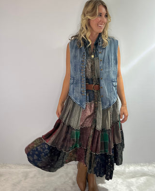 A long boho patchwork maxi duster with a hood, sleeveless design, full button front closure, drawstring ties, and tiered flowy silhouette