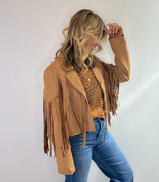 Stylish camel-colored suede jacket with long sleeves, a classic collar, and fringe detailing along the hem and sleeves. Perfect for adding a boho chic touch to any outfit