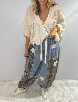Pol Elastic waist patchwork jogger pants with drawstrings, paisley and leopard prints, and crochet daisy patch details in browns and denim blue. 