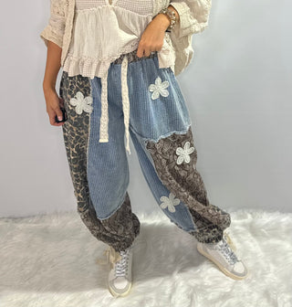 Pol Elastic waist patchwork jogger pants with drawstrings, paisley and leopard prints, and crochet daisy patch details in browns and denim blue. 
