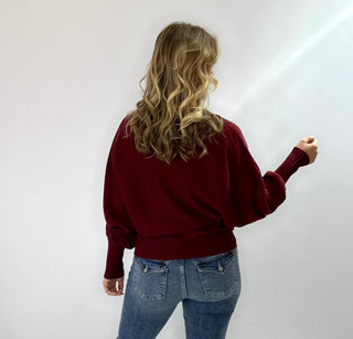 Burgundy loose knit turtleneck sweater with bat sleeves and white monogram "Merry" across the front