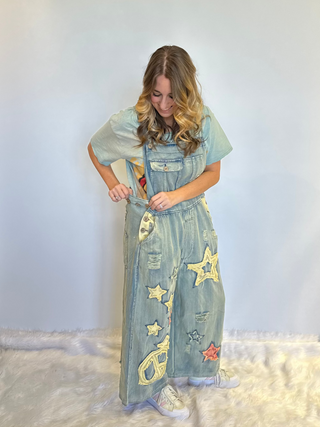 Star and Peace Patchwork denim bib overalls with oversized fit, adjustable button straps, side button closures, front bib pocket and full length silhouette