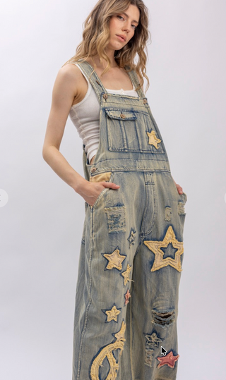 Star and Peace Patchwork denim bib overalls with oversized fit, adjustable button straps, side button closures, front bib pocket and full length silhouette